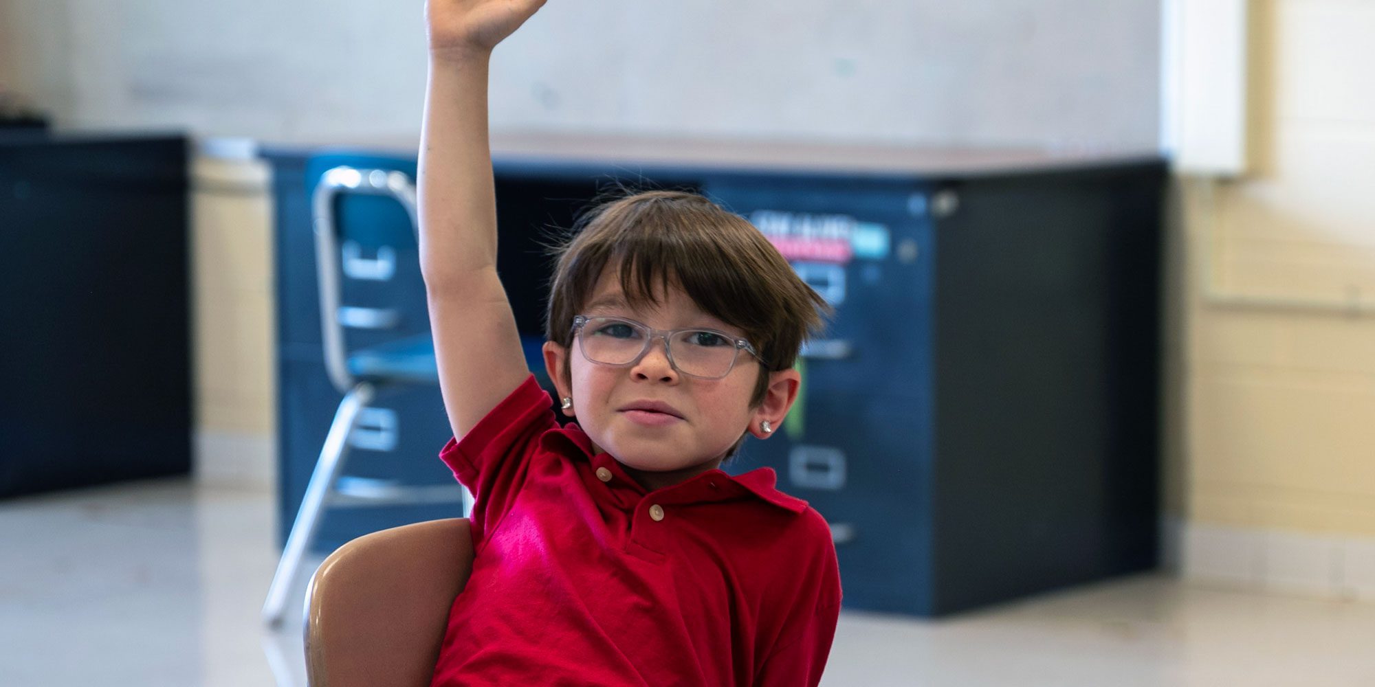 Student with glasses raising hand in classroom